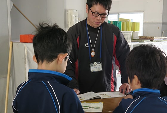 写真：佐久間先生（中央）とクイズに答える男子児童2名